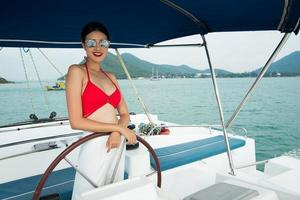 mooi Aziatisch mengen ras gebruind huid vrouw wandelen langs luxe jachten in diep oceaan, rood bikini zonnebril meisje poseren net zo mode model- in aanmeren pier onder zomer blauw lucht in vakantie vakantie foto