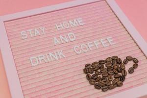 citaat blijven huis en drinken koffie Aan roze decoratief bord. kop gemaakt van koffie bonen. het voorkomen slogan het formulier covid-19 foto