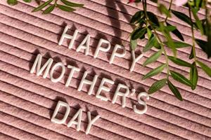 roze letterbord met citaat gelukkig moeder dag, versierd met groen bladeren Aan roze achtergrond. feestelijk groet kaart foto