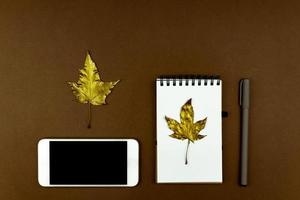 herfst zaken concept - blanco ringgebonden notitieboekje met gouden esdoorn- blad, wit smartphone en pen Aan bruin achtergrond met kopiëren ruimte foto