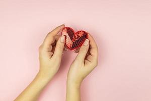 vrouw handen Holding rood pailletten hart Aan roze achtergrond. creatief minimaal lay-out met kopiëren ruimte foto