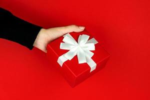 vrouw hand- Holding rood Cadeau doos Aan rood achtergrond. feestelijk creeting kaart voor vakantie. foto