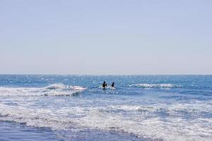 twee mannen zwemmen Aan een surfen bord in de zee of oceaan in een zonnig dag. surfing en vakantie concept. foto