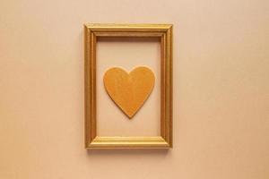 Valentijnsdag dag of bruiloft romantisch concept. gedraaid decoratief lint en gouden foto kader met houten hart Aan beige achtergrond.