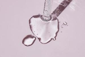 een kunstmatig Product gel of collageen serum stromen uit van een pipet met bubbels Aan roze achtergrond. foto