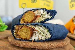 falafel belegd broodje gerold in vlak groen brood. veganistisch belegd broodje in lavash brood met groenten en gefrituurd bal of pasteitje-vormig beignet gemaakt van grond kikkererwten, fava bonen, of beide. foto