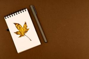 herfst zaken concept - blanco ringgebonden notitieboekje met gouden esdoorn- blad en pen Aan bruin achtergrond met kopiëren ruimte foto