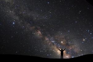 landschap met melkachtig manier, nacht lucht met sterren en silhouet van een staand sportief Mens met verheven omhoog armen Aan hoog berg. foto