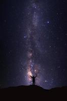 landschap met melkachtig manier heelal, sterrenhemel nacht lucht met sterren en silhouet van een staand sportief Mens met verheven omhoog armen Aan hoog berg. foto