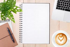 een Open blanco notitieboekje, laptop met pen en een kop van koffie Aan houten tafel. foto