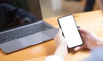 hand- vrouw gebruik makend van een telefoon, leeg scherm slim telefoon en computer Aan houten tafel top visie. foto