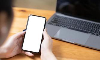 hand- vrouw gebruik makend van een telefoon, leeg scherm slim telefoon en computer Aan houten tafel top visie. foto