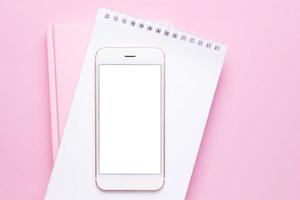 mobiel telefoon bespotten omhoog en notitieboekje Aan roze pastel tafel top visie in vlak leggen stijl. vrouw werken bureau. foto