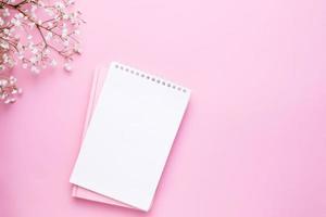 leeg notitieboekje en wit bloemen Aan roze pastel tafel top visie in vlak leggen stijl. vrouw werken bureau. foto