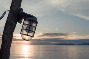 silhouet van retro straatlantaarn, lamp hangende Aan houten elektrisch pool. wijnoogst pijler met lamp. Doorzichtig leeg blauw lucht achtergrond, kopiëren ruimte. oud lantaarn foto