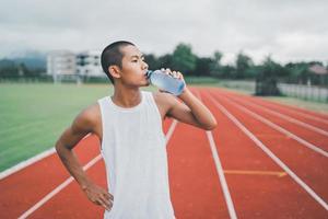 aantrekkelijk Aziatisch sport Mens loper moe en dorstig na rennen training drinken water. sport Mens concept. foto