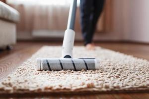 menselijk poten en een wit turbo borstel van een draadloos vacuüm schoonmaakster reinigt de tapijt in de huis foto