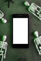 decoratief skeletten liggen in de buurt de smartphone Aan een donker achtergrond. foto