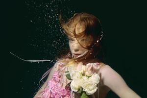 jong roodharige meisje in jurk gemaakt van rozen onderwater- foto