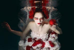 vrouw in jurk gemaakt van wit en rood rozen onderwater. fee verhaal, kunst, mode concept foto