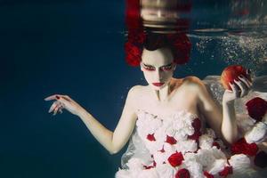 vrouw in jurk gemaakt van wit en rood rozen onderwater. fee verhaal, kunst, mode concept foto