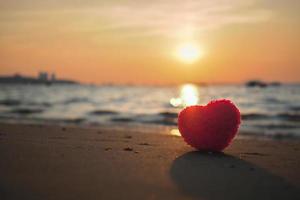 rood hart vorm Aan zand strand Bij kust met silhouet zonsondergang Aan zee voor creëren zoet lief kaart en paar poster. foto