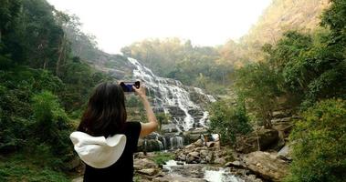 vrouw in zwart t-shirt nemen foto's van mooi waterval door smartphone. foto