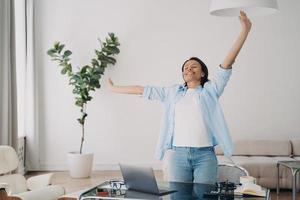 gelukkig vrouw staat uitrekken Bij werkplek, ontspannende genieten van breken na geslaagd werk Bij laptop foto