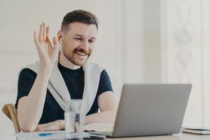 gelukkige mannelijke freelancer in draadloze oortelefoons met videogesprek terwijl hij thuis werkt foto