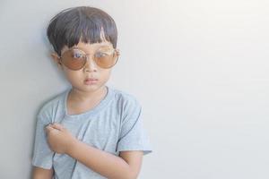 portret van een gelukkig jong jongen van Azië oorsprong in een grijs overhemd en zonnebril kijken Bij de camera foto