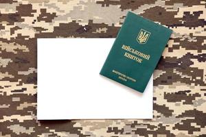 oekraïens leger ID kaart en blanco papier vel Aan kleding stof met structuur van korrelig camouflage. kleding met camo patroon in grijs, bruin en groen pixel vormen met oekraïens leger persoonlijk teken. foto