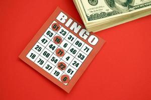 rood bingo bord of spelen kaart voor winnend chips en stack van dollar rekeningen. klassiek Amerikaans of Canadees vijf naar vijf bingo kaart Aan rood achtergrond foto