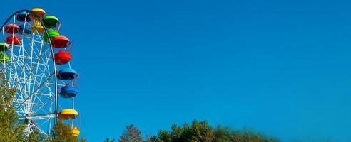 landschap van een pretpark met de top van een reuzenrad dat boven de boomtoppen tegen een blauwe lucht weergeeft. foto