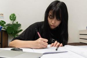 aziatisch studentenmeisje schrijft huiswerk en leest een boek aan de balie foto