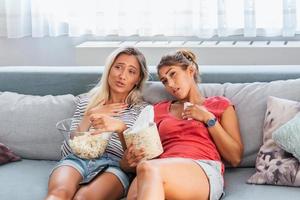 twee het beste vrienden kijk maar verdrietig film Bij huis in bed huilen aanraken. meisjes houden popcorn en TV afgelegen controle op zoek scherm romantisch film Aan televisie. Dames in pyjama- afvegen scheur gebruik makend van zakdoek foto