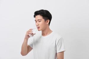 een Mens in een t-shirt en broek Aan een wit achtergrond drinken water van een glas foto