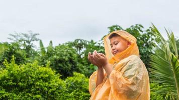 Aziatisch jongen vervelend oranje regenjas is gelukkig en hebben pret in de regen Aan een regenachtig dag. foto