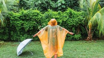 Aziatisch jongen vervelend oranje regenjas is gelukkig en hebben pret in de regen Aan een regenachtig dag. foto