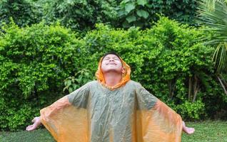 Aziatisch jongen vervelend oranje regenjas is gelukkig en hebben pret in de regen Aan een regenachtig dag. foto