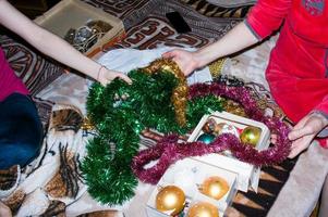 twee Dames zijn kiezen Kerstmis decoraties voor de huis boom. dames handen zijn Holding Kerstmis speelgoed en slingers. foto