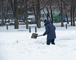 Mens met een Schep wist sneeuw buitenshuis. arbeider gedurende sneeuw verwijdering in winter stad, straat schoonmaak foto