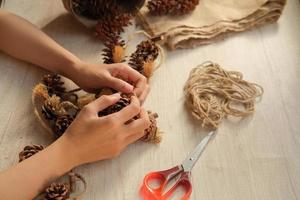 een deel van een vrouw handen maken muur ophangingen van pijnboom kegels en jute- touw foto