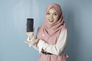 een jong Aziatisch moslim vrouw vervelend roze hijab is glimlachen terwijl tonen haar smartphone scherm foto