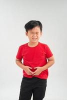 verdrietig weinig Aziatisch jongen lijden van maag pijn, Holding zijn maag, geïsoleerd Aan wit achtergrond. foto