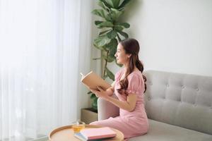 elegant Aziatisch vrouw lezing boek Bij leven kamer Aan bank. foto