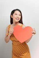 portret van aantrekkelijk Aziatisch glimlachen vrouw Holding rood hart Aan wit achtergrond foto