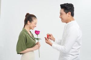 aantrekkelijk jong vrouw is staand met rozen in handen terwijl knap Mens is maken voorstel met ring in handen. foto