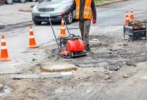 een weg onderhoud arbeider reparaties een sectie van de rijbaan in de buurt een riool mangat. foto