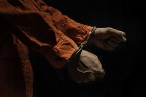 handboeien Aan verdachte crimineel in oranje gevangenis jumpsuit. wet overtreder veroordeeld naar dienen gevangenis tijd, in zwart achtergrond foto