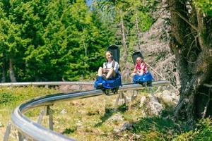 ski toevlucht berg achtbaan. twee meisjes, een achter de ander, zijn gaan naar beneden de ski helling. Woud en bomen in de achtergrond foto